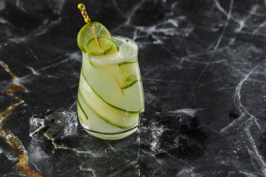 Salatalıkla süslenmiş cin kokteyli. Yeşil alkol kokteyli. Siyah arka planda bir salatalıkla