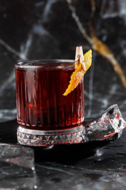 Parlak soğuk alkollü kristal bardak. Portakal suyuyla süslenmiş. Arka plan bulanık. Negroni kokteyli.