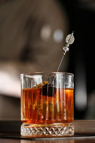 Old fashioned cocktail, consisting of Bourbon, Angostura Bitter, sugar cubes, a few drops of water, ice cubes, orange, maraschino cherry.