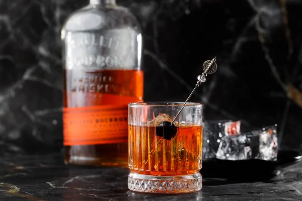 Old fashioned cocktail, consisting of Bourbon, Angostura Bitter, sugar cubes, a few drops of water, ice cubes, orange, maraschino cherry.