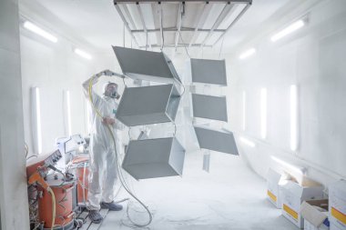 Sprey kabindeki metal ürünlerin toz tabakası. Boya kabinindeki metal parçaları boyama endüstrisi. Sprey tabancalı kapaklı işçi boya odasındaki çelik parçaları boyuyor.