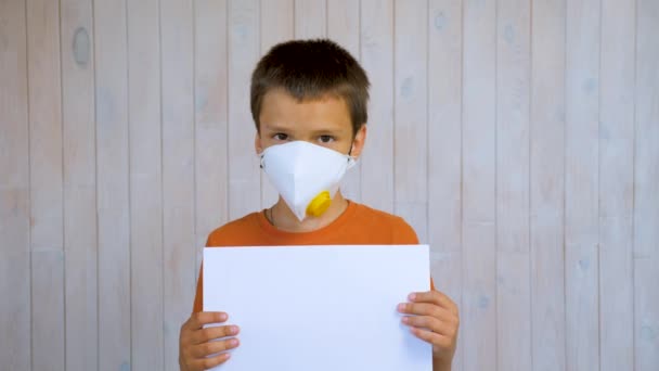 Usando máscara niño sosteniendo hoja en blanco de papel para anuncios. cámara de retrato de niño pequeño. Respirador. Chico retrato niño mirando la cámara. latino chico cabeza disparo niño retrato cara máscara protección infantil — Vídeo de stock