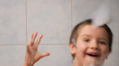 Yüzü gülüyor. Yüzü gülüyor. Çocuğu kapıyor, banyo yaptırıyor. Köpük banyosu yapan çocuk, suda yüzen eğlenceli çocuğu oynuyor. Olumlu duygular, çocuk yüzlü çocuk banyosu.