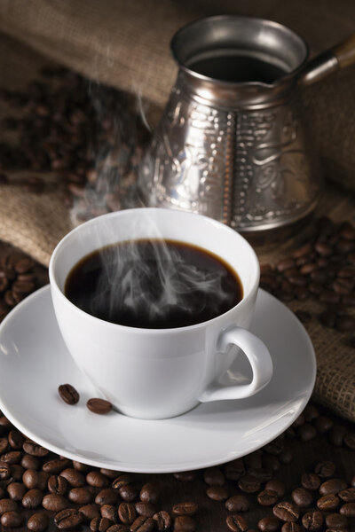 Fuming cup of coffee, coffee maker and coffee grains round them