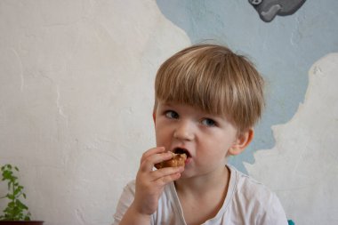 Avrupalı sarışın çocuk beyaz bir duvarın arkasında kek yiyor.