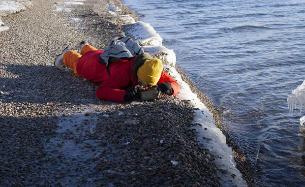 Genç bir kadın, deniz kıyısında yerde uzanmış cep telefonuyla fotoğraf çekiyor. Kışın turizm. Etkin yaşam biçimi. — Stok fotoğraf