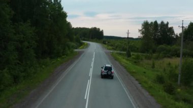 Yeşil çimenlerin arasında yol boyunca giden bir arabanın havadan görünüşü