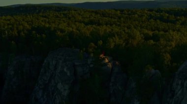 Gün batımında bir kayanın üzerinde uzanan bir kızın hava görüntüsü.