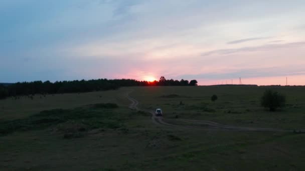 Aerial view of a car driving in nature on a field at sunset — Stockvideo