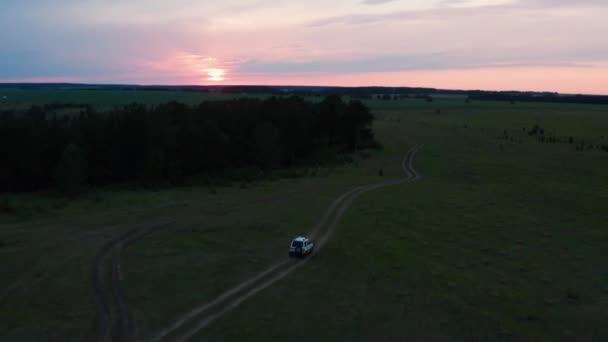 Aerial view of a car driving in nature on a field at sunset — 图库视频影像