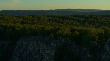 Gün batımında bir kayanın üzerinde meditasyon yapan bir kızın hava görüntüsü.