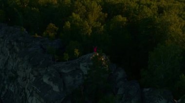 Gün batımında bir kayanın üzerinde uzanan bir kızın hava görüntüsü.