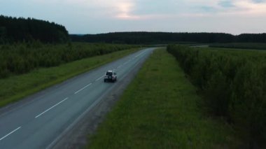 Yeşil çimenlerin arasında yol boyunca giden bir arabanın havadan görünüşü