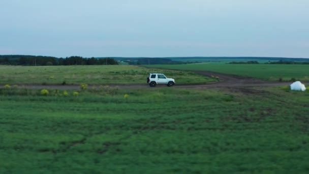 Vista aérea de un coche conduciendo en la naturaleza en un campo al atardecer — Vídeos de Stock