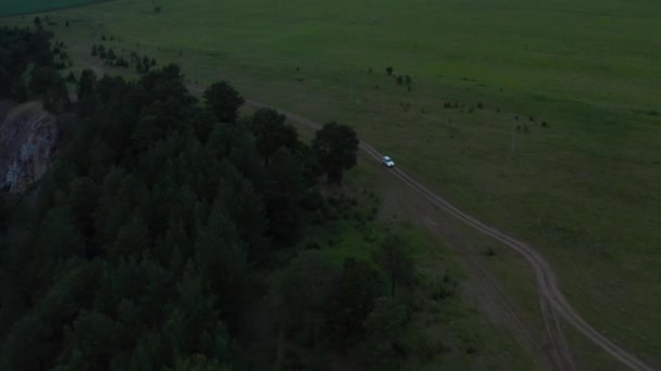 Vista aérea de un coche conduciendo en la naturaleza en un campo al atardecer — Vídeos de Stock