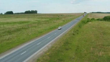 Yeşil çimenlerin arasında yol boyunca giden bir arabanın havadan görünüşü