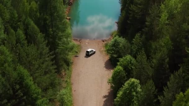 Vista aérea de um carro de viajantes na estrada perto do lago entre as árvores — Vídeo de Stock