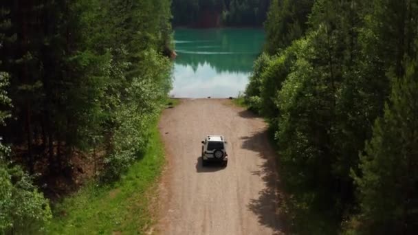 Vista aérea de um carro de viajantes na estrada perto do lago entre as árvores — Vídeo de Stock