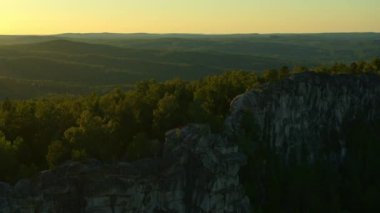Gün batımında bir kayanın üzerinde meditasyon yapan bir kızın hava görüntüsü.