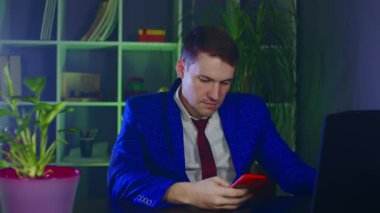 Modern iş yerinde cep telefonu kullanan düşünceli bir işadamı. Genç adam akıllı telefona bakıyor, ofisinde oturuyor..