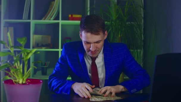 Счастливый бизнесмен с деньгами в офисе. Молодой человек с долларовыми купюрами за столом на современном рабочем месте. — стоковое видео