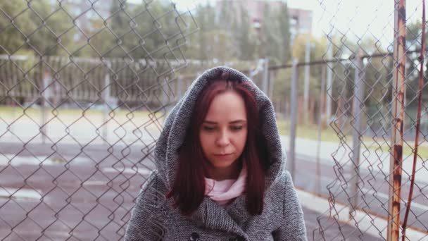 Портрет красивой женщины в сером пальто позирует возле решетчатого забора поздней осенью. — стоковое видео