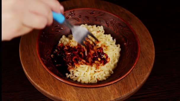Ready-made instant noodles with condiment and spicy sauce in plate on wooden board. Unrecognizable womans hand with fork shuffles ramen with additives. Close up. — Stock Video