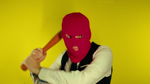 En man i rosa balaklava med baseballträ. Huligan i mask med fladdermus i händerna. En man i ett företag strikt elegant kostym med en trä fladdermus i händerna — Stockvideo