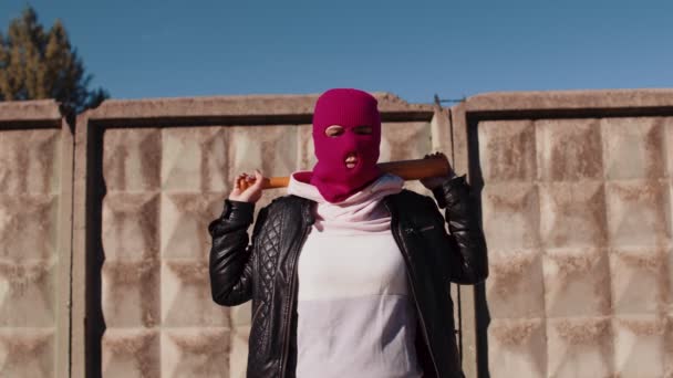 Mujer joven en pasamontañas rosa con bate de béisbol. Hooligan en máscara con murciélago en las manos. — Vídeo de stock