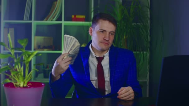 Young businessman with money in modern workplace. Serious businessperson waves money as fan, sitting in office. — Stock Video