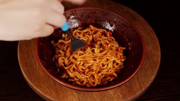 Fideos instantáneos listos con condimento y salsa picante en plato sobre tabla de madera. Mujeres irreconocibles follando ramen en un tenedor. De cerca.. — Vídeos de Stock