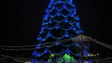 Şehir merkezinde gece gökyüzüne karşı farklı Noel oyuncakları olan Noel ağacı. Tatillerde şenlik havası yaratmak için dekoratif süslerle aydınlatılmış kozalaklı ağaç..