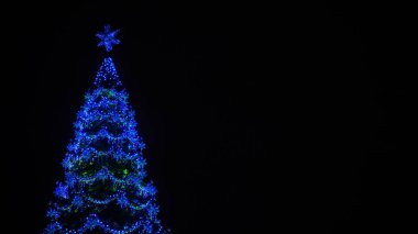 Şehir merkezinde gece gökyüzüne karşı farklı Noel oyuncakları olan Noel ağacı. Tatillerde şenlik havası yaratmak için dekoratif süslerle aydınlatılmış kozalaklı ağaç..