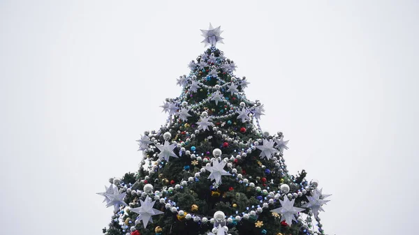Árbol de Navidad con diferentes juguetes de Navidad contra el cielo nublado en el centro. Árbol de coníferas con adornos decorativos para crear ambiente festivo durante las vacaciones. —  Fotos de Stock