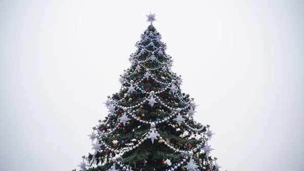 Christmas tree with different christmas toys against cloudy sky in downtown. Coniferous tree with decorative adornments to create festive mood during holidays. — Stock Photo, Image