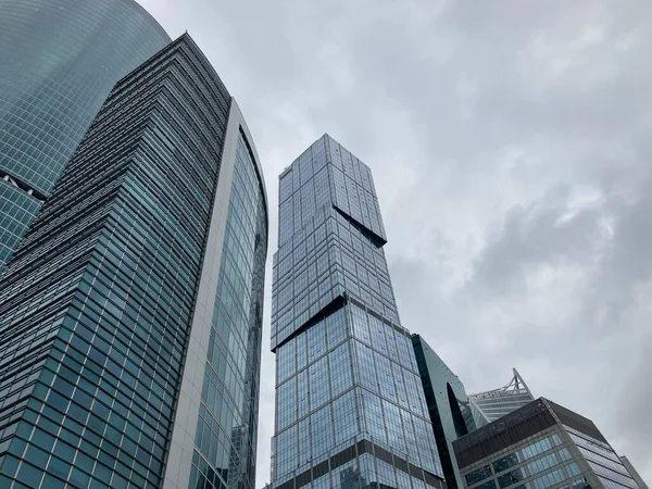 Fachada de rascacielos moderno con paredes de cristal. Desde abajo de rascacielos altos contemporáneos con paredes de vidrio contra el cielo nublado en el centro —  Fotos de Stock