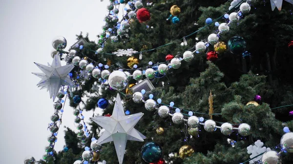 Різдвяна ялинка з різними різдвяними іграшками проти хмарного неба в центрі міста. Хвойне дерево з декоративними прикрасами для створення святкового настрою під час свят . — стокове фото
