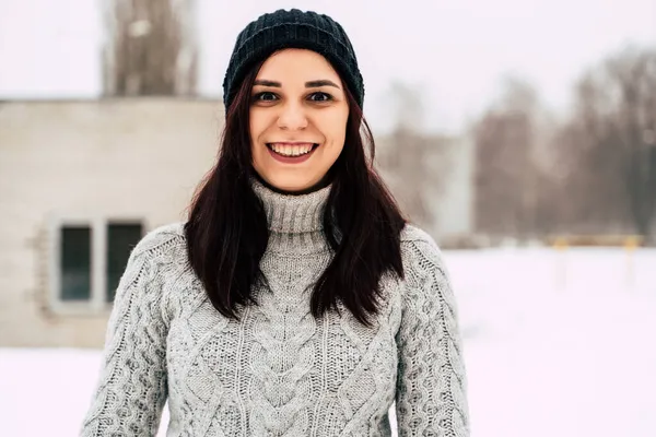 Fiatal, gyönyörű nő téli sapkával és szürke pulóverrel mosolyog és nevet, miközben kint áll télen.. — Stock Fotó