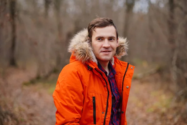Retrato de un joven con chaqueta naranja caminando en el bosque de otoño. Hombre adulto posando al aire libre en temporada de otoño. — Foto de Stock