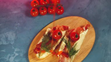 İştah açıcı bruschetts 'in ahşap tahtada, buharı giderek artan hali. Eritilmiş peynirli, pastırmalı, kiraz domatesli, dereotlu ve soslu sandviçleri mavi arka planda kes..