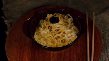 Ahşap tabakta baharatlı hazır şehriye. Tanınmayan biri baharatlı sosu tabağa ramen ile dolduruyor. Kapat..