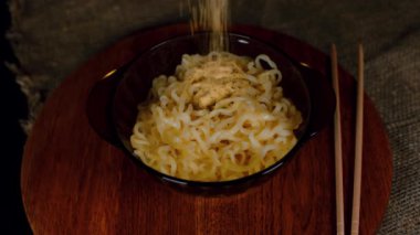 Tahta tabakta hazır erişteler. Tanınmayan kişi baharatlı sosu tabağa ramen ile serper. Kapat..