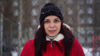 Şapkalı ve kırmızı ceketli genç bir kadın çitin arkasında dikiliyor. Dişi, kış mevsiminde çit çukurundan atlıyor. Yavaş çekim.