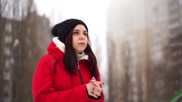 Jeune femme au chapeau et veste rouge, debout dans la rue. Brune adulte se réchauffe par temps frais sur la marche en saison hivernale. — Video