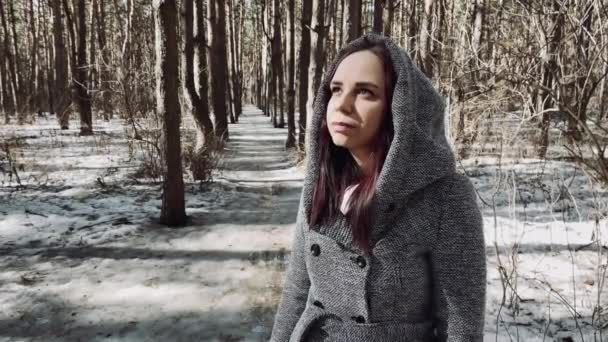 Junge schöne Frau im grauen Mantel beim Waldspaziergang. Nachdenkliche hübsche Brünette schaut weg, steht im Vorfrühling in Wäldern. — Stockvideo