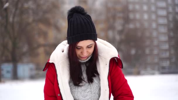 Close up of young woman in hat puts on red jacket, standing on street. Adult brunette warms in cool weather on walk in winter season. — Stock Video