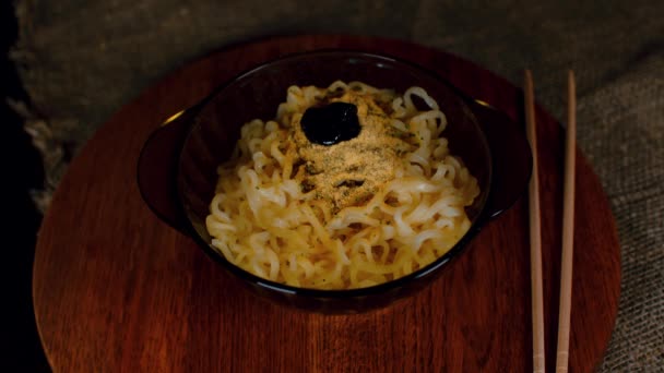 Nouilles instantanées prêtes à l'emploi avec condiment dans une assiette sur une planche de bois. Une personne méconnaissable verse de la sauce épicée dans une assiette de ramen. Gros plan. — Video