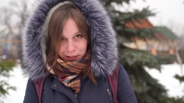 Portrét mladé ženy, smějící se na venkově v zimním období. Dospělá žena v kabátě s kapucí si s někým povídá. — Stock video