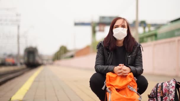 Sağlık maskeli genç bir kadın platformda tren bekliyor. Korunaklı maskeli, sırt çantalı bir kadın tren istasyonunda Coronavirus salgını sırasında tren yolculuğunu bekliyor. — Stok video