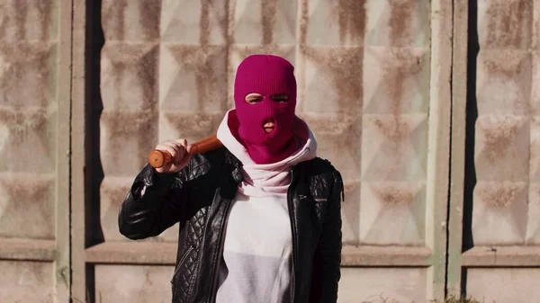 Jeune femme en cagoule rose avec batte de baseball. Hooligan en masque avec chauve-souris dans les mains. — Photo
